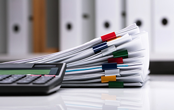 A calculator, some paperwork and a group of binders in the background.