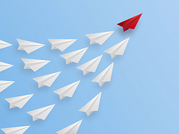 A group of white paper airplanes following a red one.