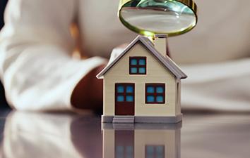 Person examining a toy house with a magnifying glass.